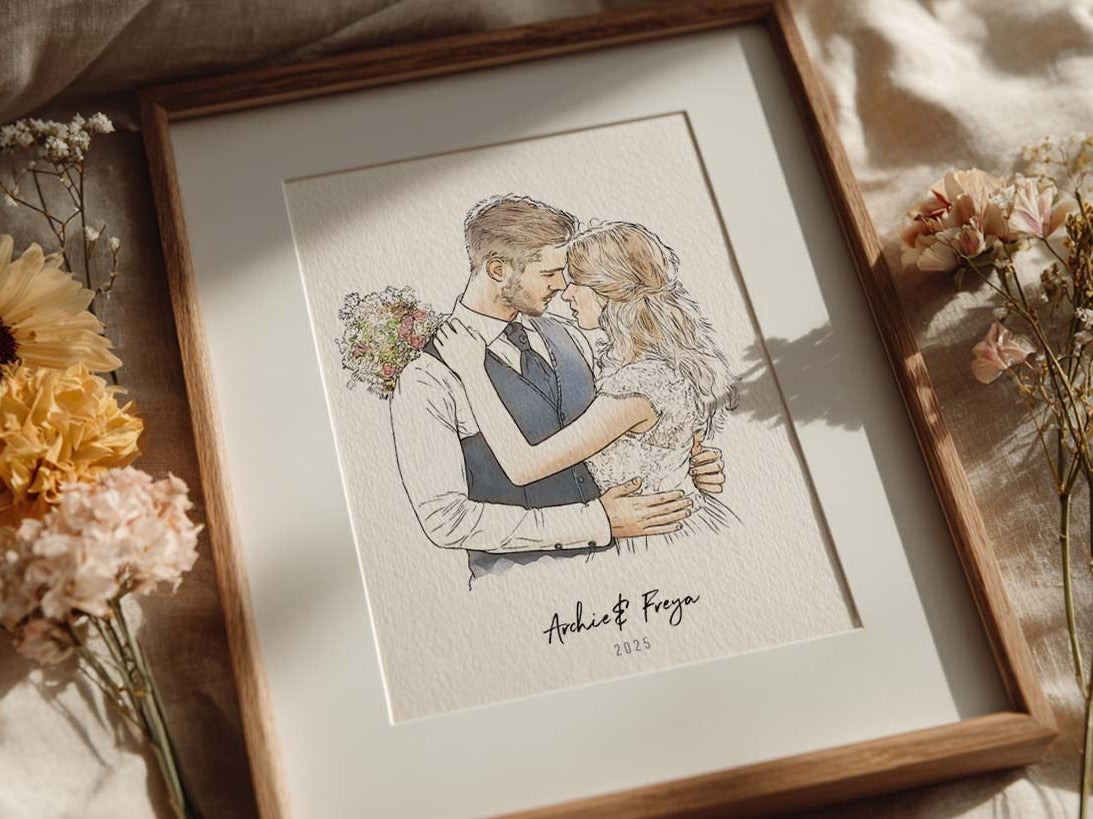 Framed personalized wedding portrait of a couple embracing, surrounded by dried flowers on soft linen bedding